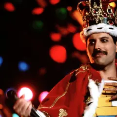 Freddie Mercury w koronie i czerwonym płaszczu, śpiewający swoje legendarne piosenki.