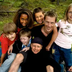 En grupp glada barn och en vuxen njuter av en dag i skogen. De ser ut som riktiga ola wild kids, redo för äventyr.