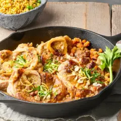 Herzhaftes Ossobuco alla Milanese in Gusseisenpfanne, garniert mit Zitronenzeste und Kräutern, daneben eine Schüssel Reis mit Erbsen.