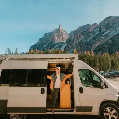 Une femme sort de son fourgon aménagé, profitant d'une vue spectaculaire sur les montagnes. Une image qui pourrait bientôt devenir un souvenir, car les fourgons aménagés vont être interdits.