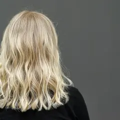 Widok z tyłu na falowane, blond włosy kobiety na ciemnym tle.