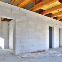 Wnętrze domu w budowie, ściany z bloczków suporeks, widoczne drewniane belki stropowe.