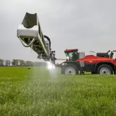Czerwony opryskiwacz rolniczy pracuje na zielonym polu, wykonując oprysk po deszczu.