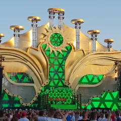 Złota, słoneczna scena festiwalowa z zielonymi światłami, gdzie jest sunrise, otoczona tłumem ludzi.