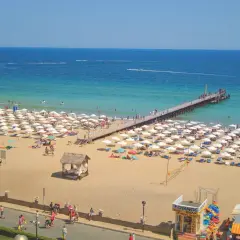 Słoneczny Brzeg, Bułgaria: plaża pełna białych parasoli, molo i turystów cieszących się słońcem i morzem.