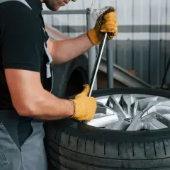 Mechanik w żółtych rękawiczkach używa klucza do opony, pokazując, jak ściągnąć oponę z felgi domowym sposobem.