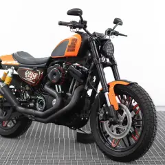 Harley Davidson custom con sella nera, serbatoio arancione e dettagli "Garage". Motore potente e ruote personalizzate.