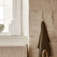 Deux patères ondulées en laiton alliage, l'une tenant une serviette verte, sur un mur texturé.