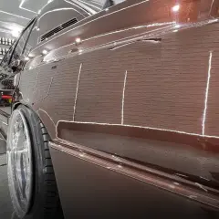 Błyszczący, brązowy lakier samochodu z odbiciami świateł i fragmentem felgi.