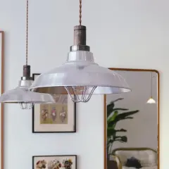 Dos lámparas de techo industriales plateadas cuelgan sobre un sofá vintage reflejado en un espejo.