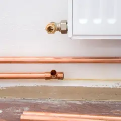Installazione di tubi in rame per il riscaldamento, con un raccordo a T e una connessione al radiatore. La coibentazione dei tubi riscaldamento è fondamentale per l'efficienza.