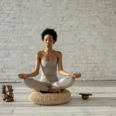 Mujer meditando en postura de loto, con los ojos cerrados y las manos en mudra. A su lado, una figura de bronce y un cuenco tibetano, elementos que invitan a la introspección y a la repetición de **palabras mantra**.