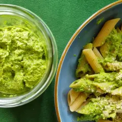Pesto z liści rzodkiewki w słoiku obok talerza penne z tym zielonym sosem i startym parmezanem.