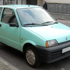 Jasnozielony Fiat Cinquecento zaparkowany na ulicy.