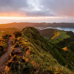 Magnifique paysage des Açores au coucher du soleil, avec un sentier serpentant sur une crête verdoyante menant à un lac paisible.