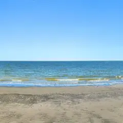 Vaste étendue de sable et de mer au Lido degli Estensi sous un ciel bleu clair. Des vagues douces caressent le rivage.