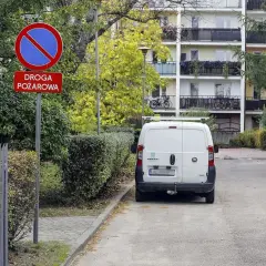 Znak "zakaz zatrzymywania się" i "droga pożarowa" obok białego vana. Kierowca może spodziewać się mandatu za złe parkowanie od straży miejskiej.
