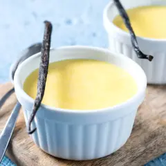Deliciosas natillas de plátano, cremosas y con un toque de vainilla, servidas en ramequines blancos sobre una tabla de madera.