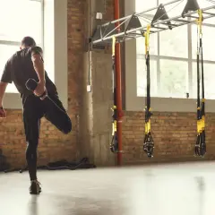 Hombre estirando la pierna, un ejemplo de la definición de calentamiento en un gimnasio con ladrillos y TRX.