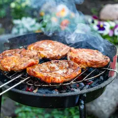 Saftige Steaks brutzeln auf dem Grill. Tolle Grill Tipps für ein perfektes Ergebnis. Rauch steigt auf, Blumen blühen im Hintergrund.
