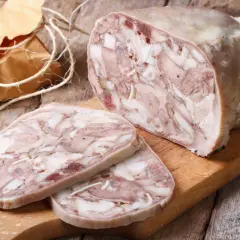 Kawałek salcesonu, z czego jest zrobiony, widać kawałki mięsa i tłuszczu. Pokrojone plastry leżą obok.