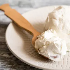 Un cucchiaio di legno raccoglie del cremoso mascarpone da un piatto. Si può congelare il mascarpone per conservarlo più a lungo.