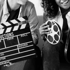 Dwie osoby z klapsem filmowym i rolką taśmy filmowej. Zastanawiasz się, ile zarabia reżyser filmowy?