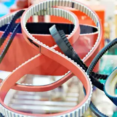 Plusieurs courroies de distribution, certaines rouges, d'autres noires, sont présentées en gros plan. Le courroie de distribution prix varie selon le modèle.