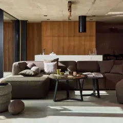 Nowoczesny salon w stylu bauhaus z dużą, narożną sofą, drewnianymi panelami i betonowym sufitem.