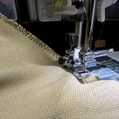 Sewing a zigzag stitch on a tan fabric to prevent fraying. This technique helps keep edges neat, unlike how some flannel might fray.