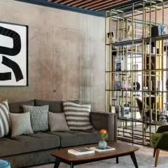 Sofá gris con cojines decorativos, mesa de centro y estantería dorada en un lobby de Radisson Collection.