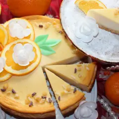Pyszny sernik pomarańczowy, udekorowany plasterkami pomarańczy i białymi kwiatami. Idealny na deser.