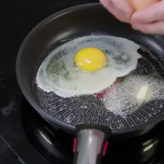 Un œuf frit cuit dans une poêle avec du beurre qui fond. Le jaune est encore coulant.