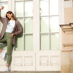 Elegancka kobieta w brązowym kardiganie i zielonych spodniach pokazuje, jak nosić kardigan na co dzień.