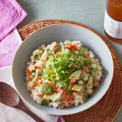 Miseczka ryżu z awokado, pomidorem i ogórkiem, polana sosem. Obok butelka z napisem "zaprawa do sushi".