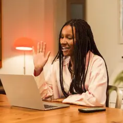 Uśmiechnięta dziewczyna z warkoczami wita się przez laptopa, ucząc się, ile słów ma język angielski.