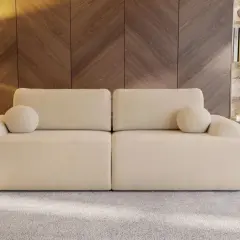 Eine cremefarbene Couch mit runden Kissen, die zum Entspannen einlädt. Sie steht vor einer Holzwand und einem Regal mit Büchern und Deko.