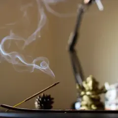 El humo del incienso se eleva en espirales blancas, creando un ambiente sereno junto a una figura dorada y una tetera decorada.