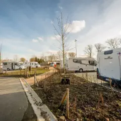 Vue d'une aire camping car Bruges avec plusieurs véhicules stationnés sous un ciel bleu.