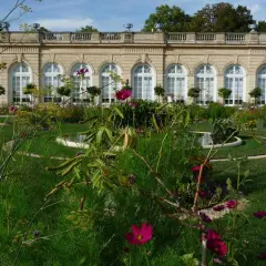 Jardin fleuri devant un bâtiment classique, avec des arches et des fenêtres, au Bois de Boulogne.