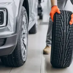 Mechanik w pomarańczowych rękawicach prezentuje nową oponę asymetryczną obok samochodu.