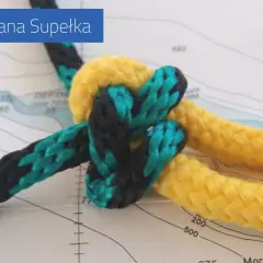 Węzeł na końcu liny, żółtej i czarno-zielonej, na tle mapy morskiej. Akademia Pana Supełka.