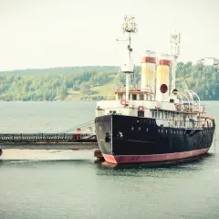 Stary statek "Angara" cumuje przy nabrzeżu. W tle zielone wzgórza i spokojna woda. Port nad Angarą.
