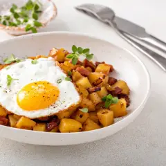 Un œuf au plat sur des pommes de terre sautées avec des lardons, une idée parfaite avec quoi accompagner des œufs pour un repas savoureux.