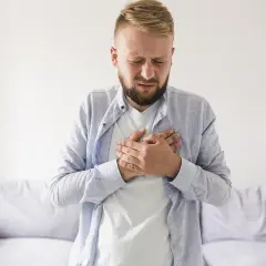 Mężczyzna z rękami na klatce piersiowej, cierpiący z powodu odbijania po jedzeniu.