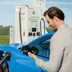 Mężczyzna sprawdza na telefonie koszt ładowania samochodu elektrycznego przy stacji Moja Energia.
