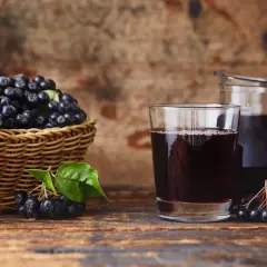 Szklanka i dzbanek z nalewką z aronii mrożonej, obok koszyk pełen świeżych owoców.
