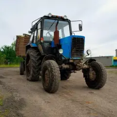 Niebieski traktor z przyczepą pełną siana, gotowy do pracy. Traktorzysta pewnie zaraz ruszy w pole.