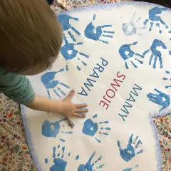 Dziecko tworzy kolaż z odcisków dłoni na sercu z napisem "Prawa swoje mamy".