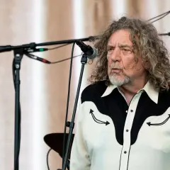 Robert Plant, jeden z legendarnych członków Led Zeppelin, na scenie z charakterystyczną fryzurą i koszulą.